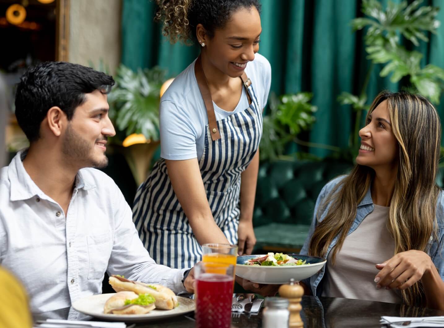 A waitress serves food to two diners in a restaurant, showcasing the efficiency of genius software in action