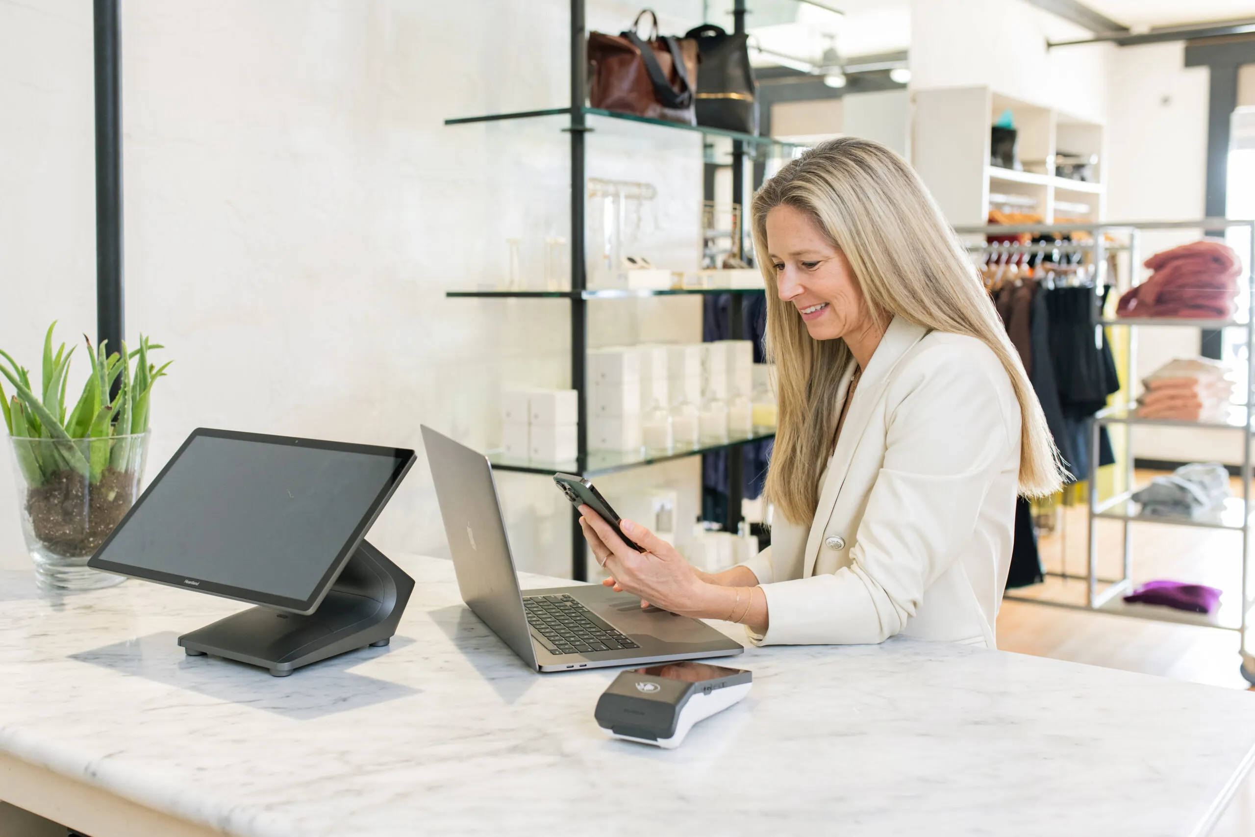 Business owner managing her boutique with a POS system, laptop, and smartphone at the counter