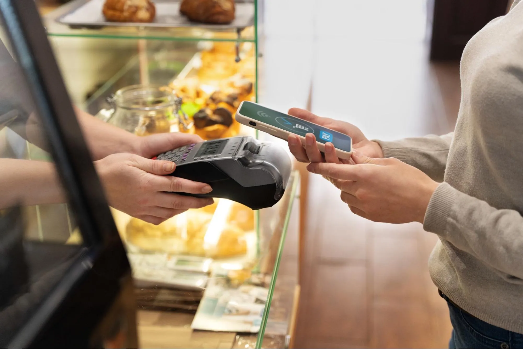 Store employee processing a transaction on a modern POS terminal, with a payment device and receipt printer visible on a wooden counter