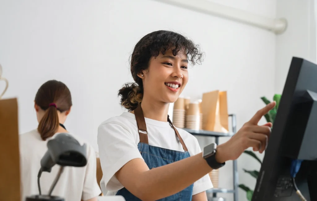 a woman manages a cash register, highlighting a specialty food POS system in a lively retail environment.