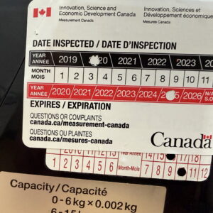 Measurement Canada examination sticker on a legal-for-trade scale, with punched inspection and expiry dates and capacity label below.