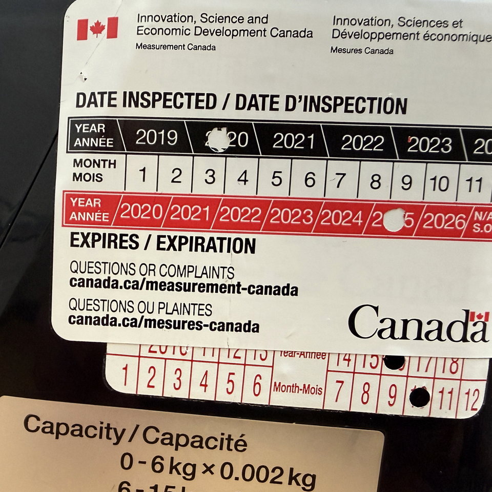 Measurement Canada examination sticker on a legal-for-trade scale, with punched inspection and expiry dates and capacity label below.