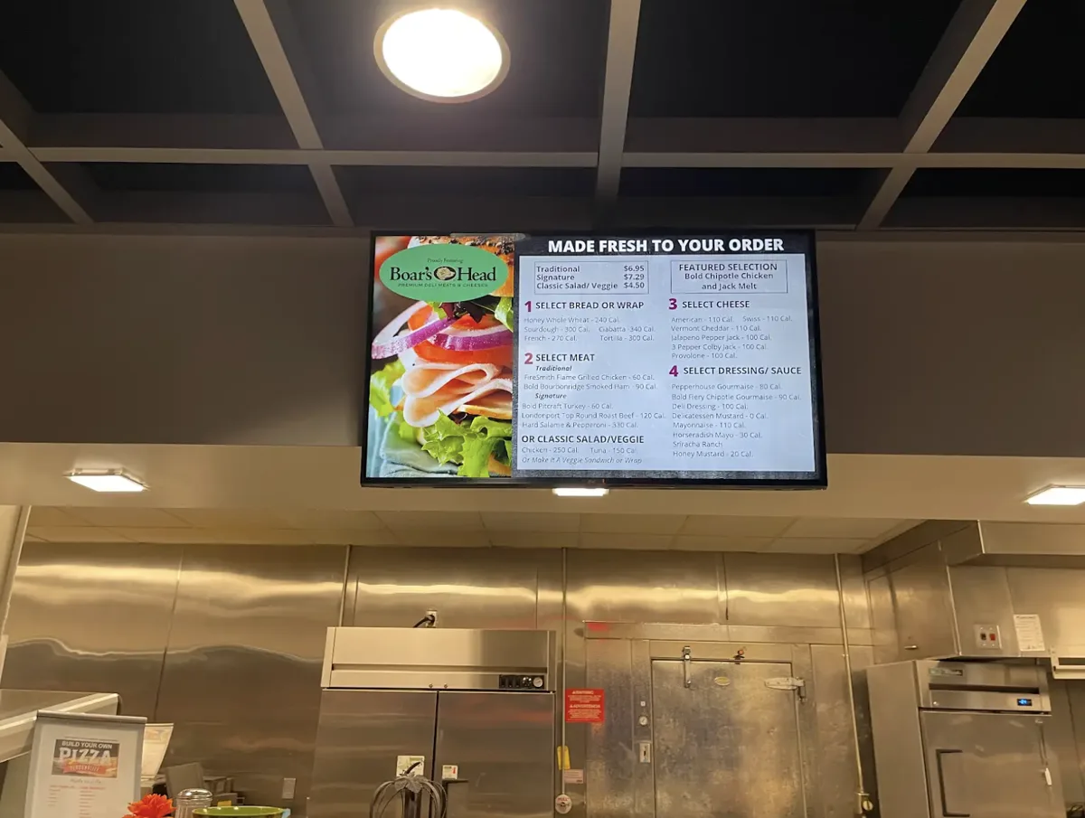 Ceiling-mounted Genius digital menu board above a made-to-order food counter
