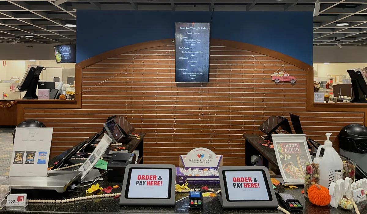 Genius Restaurant POS stations at a caf&eacute; counter with a portrait digital menu board on the wall
