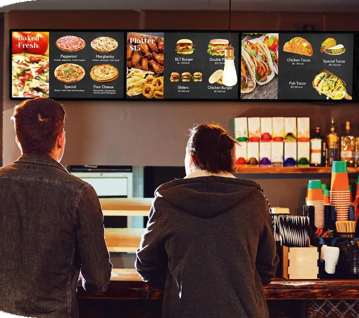 Guests ordering under a row of Genius digital menu boards at a restaurant counter